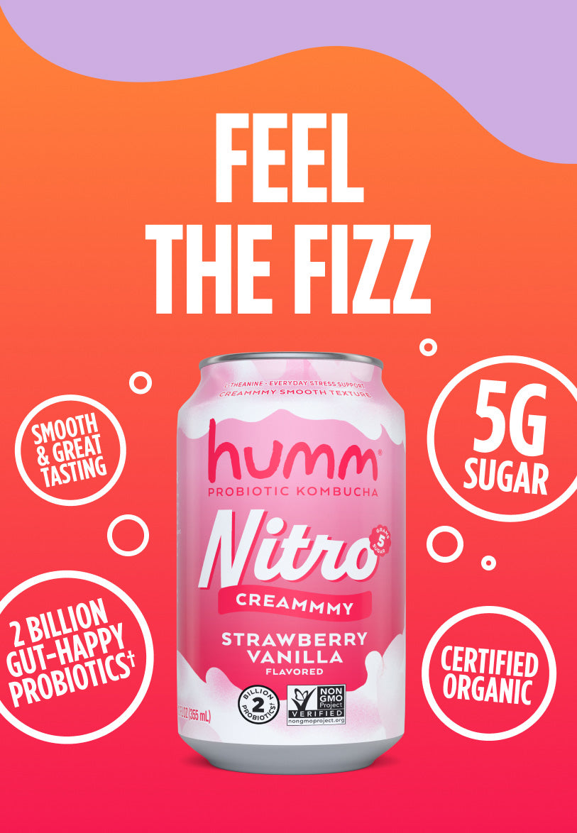 A promotional image for Humm Nitro Probiotic Kombucha in Creamy Strawberry Vanilla flavor. The background is a gradient of orange and purple with the text "FEEL THE FIZZ" in large white letters at the top. A can of the kombucha is centered, with a pink and white design. Surrounding the can are circular badges highlighting features: "VITAMIN B12," "30% LESS SUGAR*," "2 BILLION HAPPY GUT-HAPPY PROBIOTICS+," and "CERTIFIED ORGANIC." The can also notes "5g SUGAR" and mentions benefits like L-theanine for stress